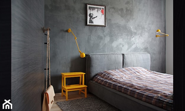 szara ściana w sypialni, szare łóżko, żółta lampa ścienna, żółta szafka nocna, pościel w kratę