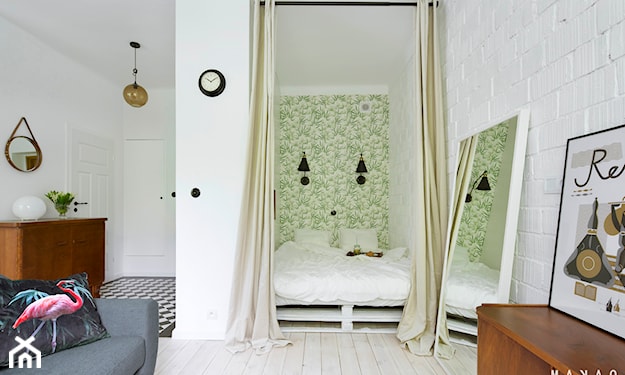 łóżko z palet za zasłoną, zielona tapeta, biała podłoga z drewna, szara sofa, drewniana komoda