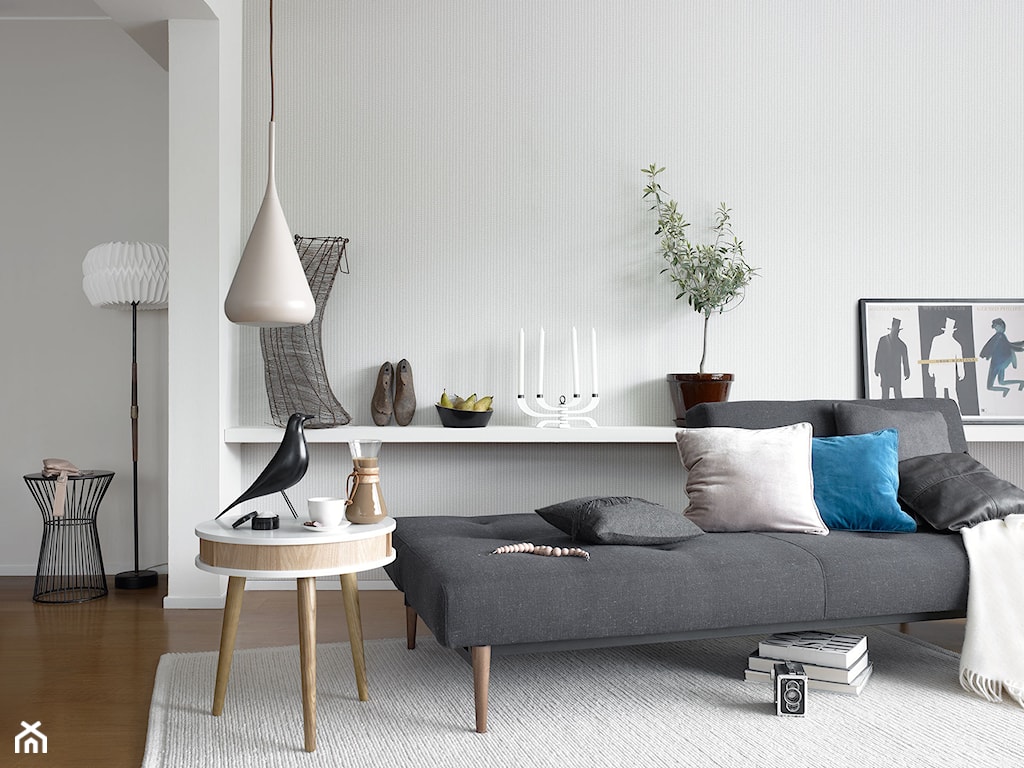 szara sofa, kremowy dywan, niebieska poduszka, biały koc, drewniany stolik, biała lampa wisząca