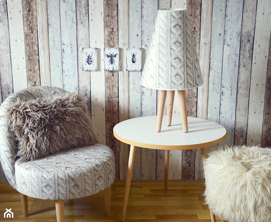 okrągły stolik z drewna, drewniana lamperia, ilustracje owadów na ścianie, szara poduszka z długim włosiem