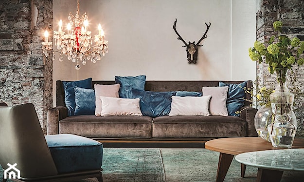 brązowa sofa, beżowa ściana, welurowe poduszki, kryształowy żyrandol, okrągły stolik z drewna