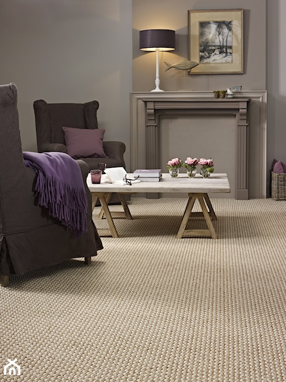 beżowy dywan, szary fotel, wiklinowy kosz, fioletowy koc, biały stolik