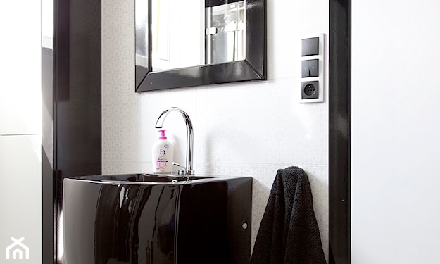 biała ściana, czarna umywalka z postumentem, lustro z czarną ramą