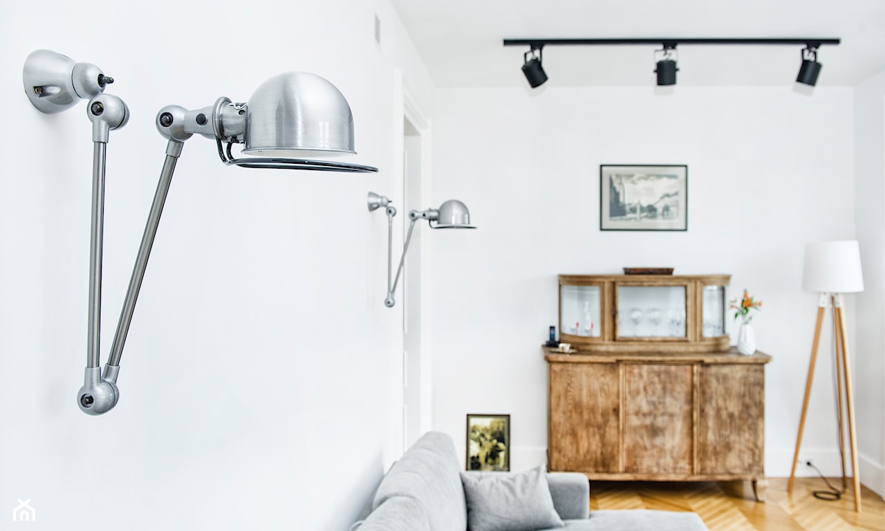 salon w stylu eklektycznym, białe ściany, metalowe lampy ścienne, drewniana komoda, drewniana lampa podłogowa z białym abażurem