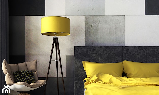 szare łóżko, betonowe płytki ścienne, lampa podłogowa z żółtym abażurem