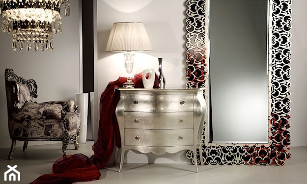 srebrna komoda, czerwony koc, fotel na nóżkach ze srebrnymi zdobieniami, kryształowy żyrandol