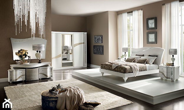 biała rama łóżka, kryształowy żyrandol, asymetryczne lustro, biała szafka nocna, beżowy dywan z długim włosiem