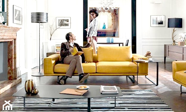 żółta sofa, dywan w biało-czarne paski, lampa podłogowa ze srebrnym karniszem
