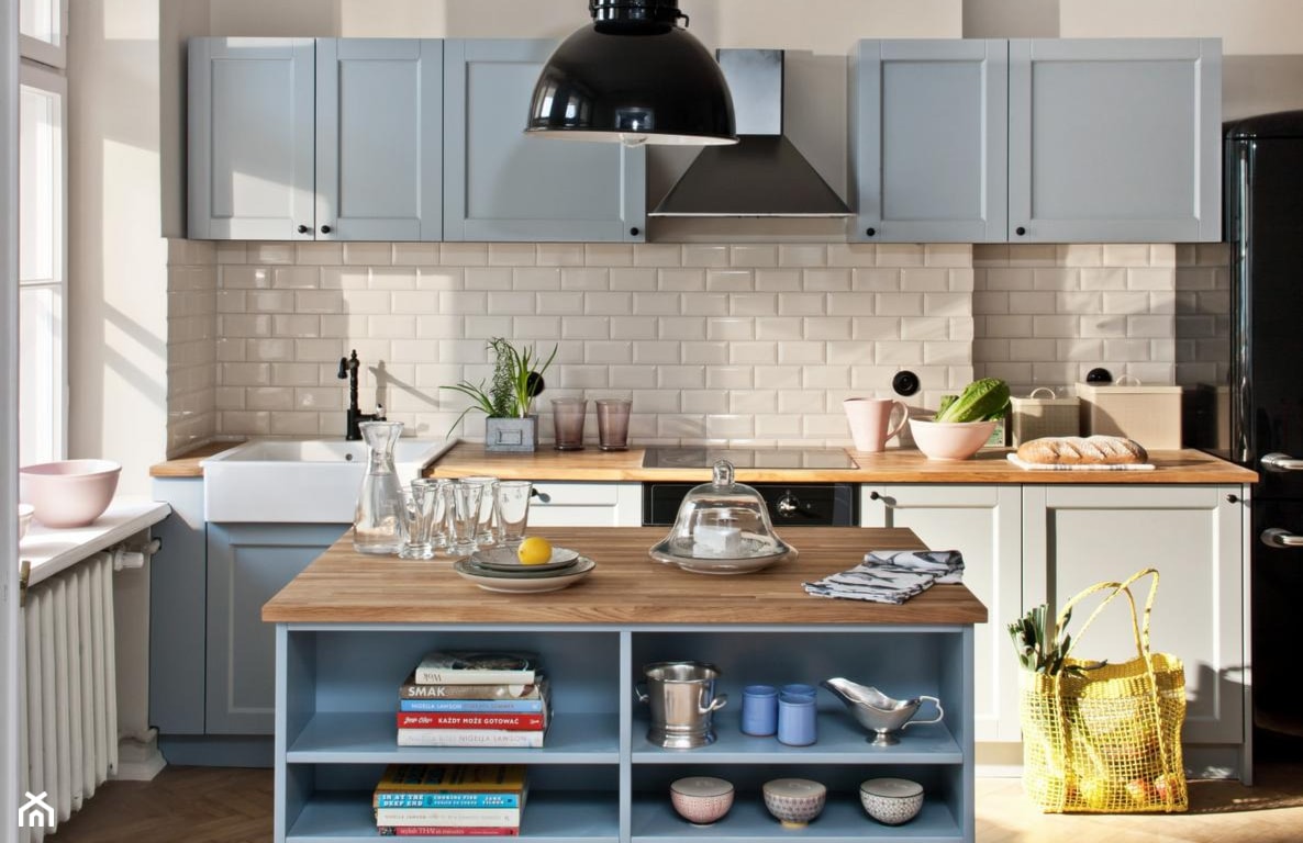 białe kafelki w kuchni, drewniany blat kuchenny, błękitne szafki kuchenne, czarna lampa wisząca