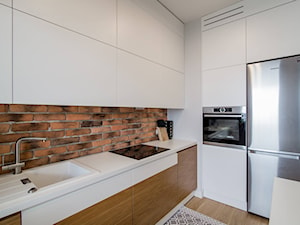 RYDYGIERA - Średnia otwarta z salonem biała z zabudowaną lodówką z nablatowym zlewozmywakiem kuchnia w kształcie litery l - zdjęcie od Qbik Design