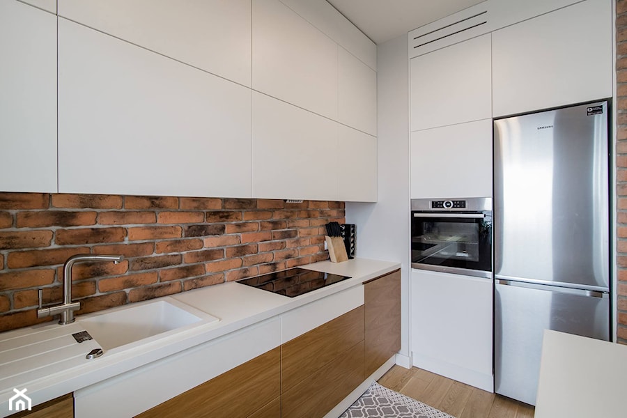 RYDYGIERA - Średnia otwarta z salonem biała z zabudowaną lodówką z nablatowym zlewozmywakiem kuchnia w kształcie litery l - zdjęcie od Qbik Design