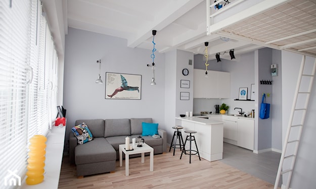 szara sofa narożna, drewniana podłoga, biały stolik, lampa żarówka na niebieskim kablu
