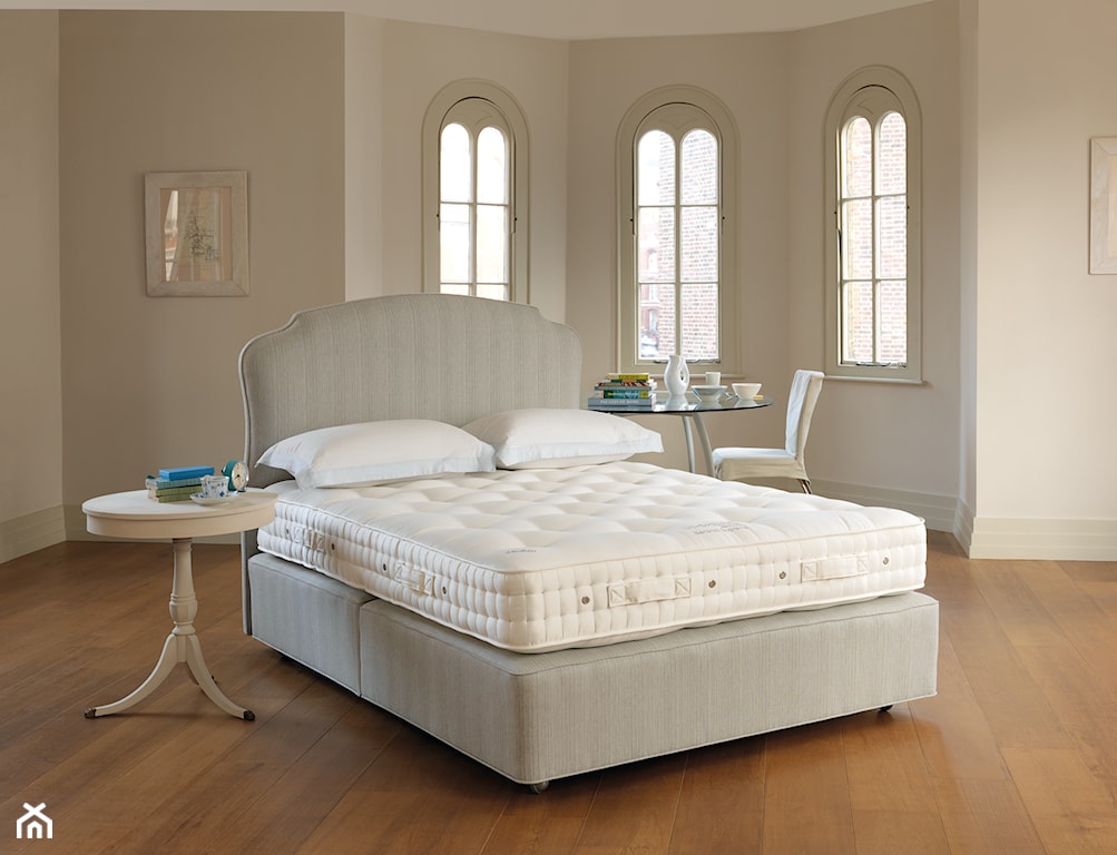 drewniana podłoga, beżowe łóżko z wysokim zagłówkiem, biały okrągły stolik