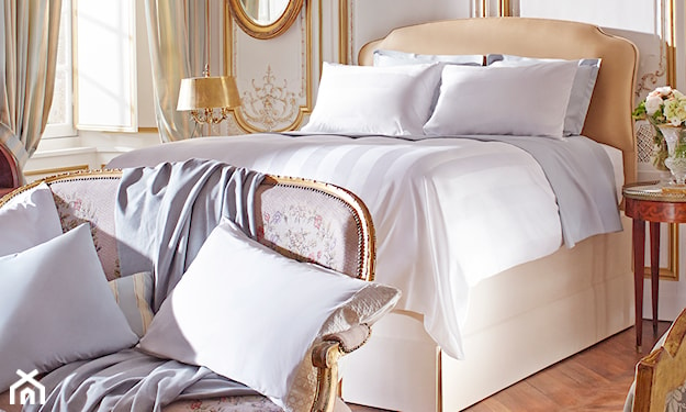 sypialnia w stylu glamour, wysokie beżowe łóżko, sofa ze złotymi zdobieniami, drewniana podłoga