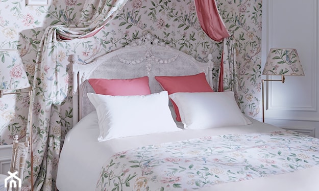 białe łóżko z ozdobnym zagłówkiem, ściana w drobne kwiatki, lampa podłogowa z abażurem w kwiatki