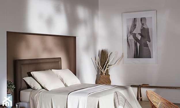 brązowe łóżko z wysokim zagłówkiem, wiklinowy fotel, kremowa pościel