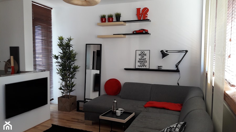 szary narożnik w małym salonie z białymi ścianami uzupełniony czerwonymi dekoracyjami - zdjęcie od Atelier 37 | architektura & projektowanie wnętrz