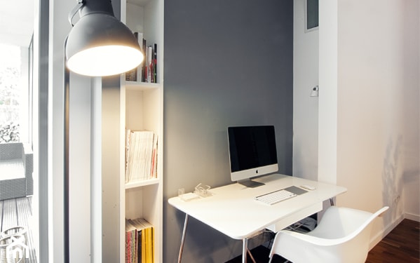 białe biurko na metalowych nogach, biała lampa podłogowa, szara ściana