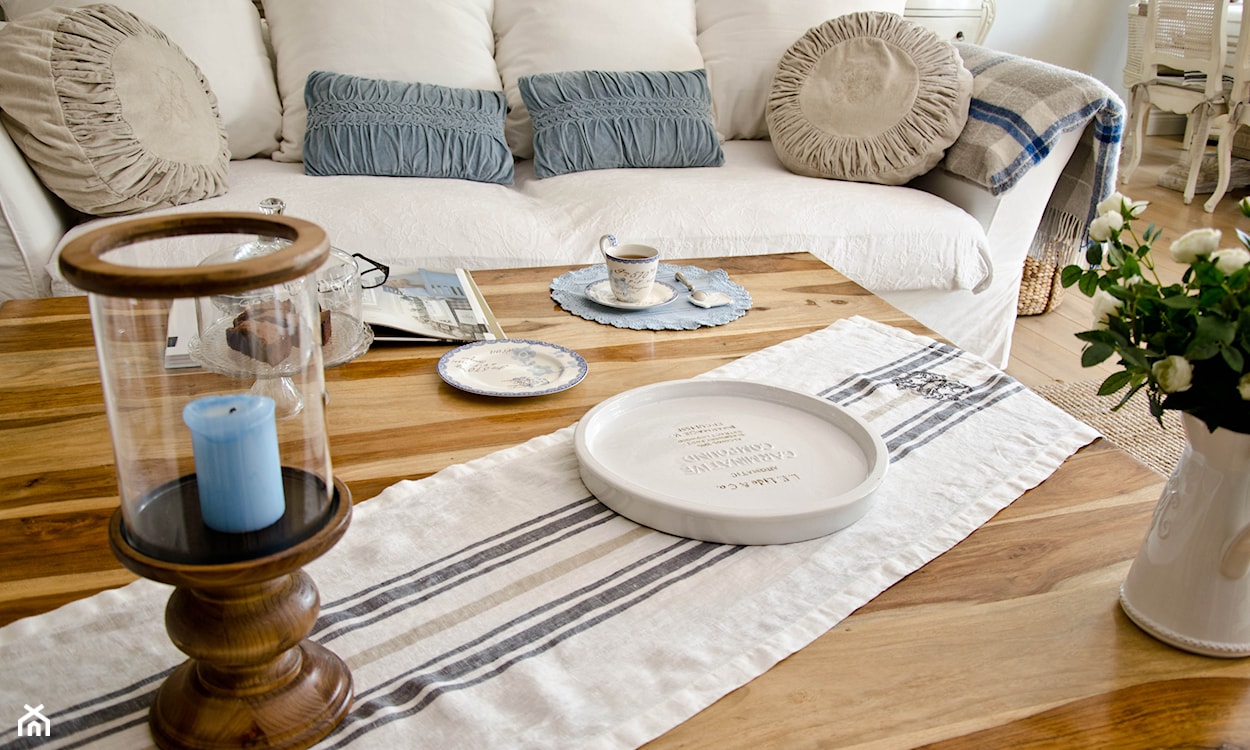 drewniany stół, beżowa sofa, niebieskie poduszki z marszczeniami, drewniany świecznik