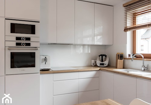 Nowoczesna biała kuchnia z drewnianym blatem - Średnia otwarta biała z zabudowaną lodówką z podblatowym zlewozmywakiem kuchnia w kształcie litery l z oknem, styl nowoczesny - zdjęcie od pracowniadebina