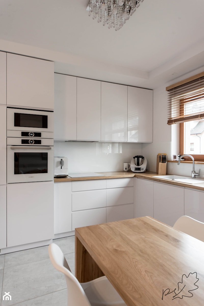 Nowoczesna biała kuchnia z drewnianym blatem - Średnia otwarta biała z zabudowaną lodówką z podblatowym zlewozmywakiem kuchnia w kształcie litery l z oknem, styl nowoczesny - zdjęcie od pracowniadebina
