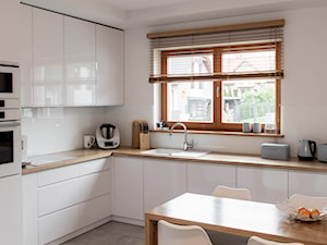 Nowoczesna biała kuchnia z drewnianym blatem - Duża otwarta biała z zabudowaną lodówką z podblatowym zlewozmywakiem kuchnia w kształcie litery l z oknem, styl nowoczesny - zdjęcie od pracowniadebina