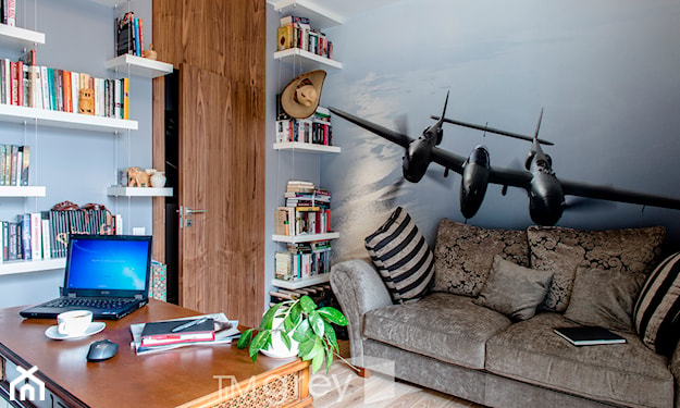 drewniana ściana, ilustracja samolotu na ścianie, szara sofa, drewniane biurko, poduszka w pasy
