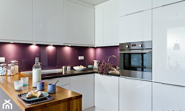 białe meble kuchenne, czarny blat, fioletowe szkło w przestrzeni między szafkami